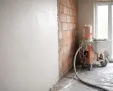 Maszyna do tynkowania nakłada tynki cementowo wapienne na ścianę z cegły.