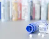 Flacons de granules homéopathiques, certains en arrière-plan floutés. Un tube bleu ouvert laisse échapper quelques billes blanches. Une solution naturelle pour la dermite séborrhéique, comme une huile essentielle, pourrait être contenue dans ces remèdes.