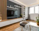 Nowoczesny salon z lamelami inspiracje: drewniane panele, szara ściana z TV, białe meble i zielona kanapa tworzą przytulną przestrzeń.