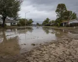 Rue résidentielle inondée, avec des maisons et des voitures. Le sol craquelé suggère une sécheresse suivie d'une forte pluie. Suis-je en zone inondable ?
