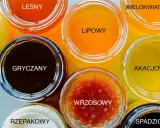 Siedem słoików z różnymi rodzajami miodów: leśny, gryczany, lipowy, wrzosowy, wielokwiatowy, akacjowy i spadziowy.