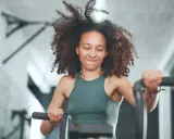 Frau mit lockigem Haar trainiert intensiv auf einem Fahrrad. Sie gibt alles, was ist HIIT – High Intensity Interval Training.