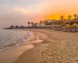 Strand in Tunesien im Oktober: Sanfte Wellen, Palmen und Liegestühle unter einem warmen Sonnenuntergang. Perfektes Wetter für einen entspannten Urlaub.