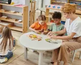 Maestra ayuda a niños de 3-4 años con rompecabezas, abordando posibles problemas de conducta con paciencia y actividades educativas.