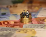 Dos figuritas sentadas en monedas de oro sobre billetes de euros. Reflexionan: como puedo cotizar los años que me faltan.