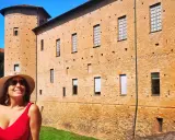 Donna sorridente con cappello di paglia davanti a un castello di mattoni rossi. Un'idea per cosa vedere a Piacenza in un giorno.