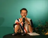 Un homme avec une écharpe tricolore, prêt à parler. Il est entouré de micros, peut-être pour un discours plein de langue de bois.