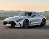 Un elegante Mercedes GTR plateado descansa en una carretera desierta, con montañas onduladas al atardecer de fondo.