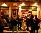 Menschen versammeln sich vor einem beleuchteten Lokal in Bairro Alto. Ein Mann hält ein Glas, andere unterhalten sich.