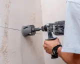 Persona taladra hormigón con una broca de corona. La marca en la pared indica dónde perforar.