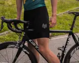 Kolarz w czarnych spodenkach i zielonej koszulce przygotowuje się do treningu kolarskiego. Rower szosowy Cannondale czeka na jazdę.