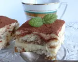 Pyszne tiramisu bezglutenowe, posypane kakao i udekorowane listkiem mięty, czeka na łyżeczkę.