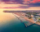 Alba rosa sul cattolica mare, con la costa e le colline sullo sfondo. Una barca solca le acque calme.