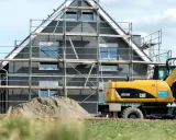 Ein Haus im Bau mit Gerüst und einem Bagger. Die bauseitigen Leistungen sind im vollen Gange.