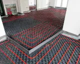 Instalación de suelo radiante con tuberías rojas sobre paneles negros, preparado para aerotermia.