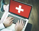 Osoba pisząca na laptopie z flagą Szwajcarii na ekranie.