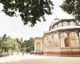 Ein sonniger Tag im Retiro Park. Menschen spazieren vor dem Palacio de Cristal, einem beeindruckenden Glaspalast.