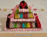 Una pirámide de tartas de gominolas, con capas de malvaviscos rosas, gominolas de colores y frutos rojos en la cima.