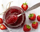Glas mit Erdbeermarmelade, gesüßt mit Xylit, daneben frische Erdbeeren und ein Löffel Marmelade.
