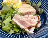 Ein perfekt gegrilltes Thunfischsteak, in Scheiben geschnitten, serviert mit frischem Salat, Zitrone und Dill auf einem blauen Teller.