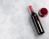 En flaska tamaral vin och ett glas rött vin på ett grått, stenig bakgrund.