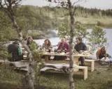 Vänner njuter av en måltid vid en sjö, en hyllning till det ätbara landet Sverige.
