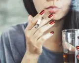 Frau mit roten Nägeln raucht Zigarette und hält Glas. Mögliche Auswirkungen auf Progesteron und Rauchen.