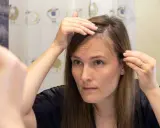 Kobieta w łazience sprawdza swoje włosy, zastanawiając się, jak wygładzić włosy.