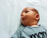 Noworodek z lekkim kręczem szyi i asymetrią twarzy, w szarym body z napisem "mom".