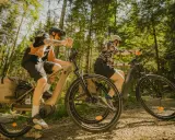 Dwie osoby na rowerach elektrycznych przemierzają leśną ścieżkę. Różne rodzaje rowerów elektrycznych pozwalają na komfortowe wycieczki.