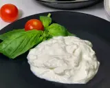 En krämig hög av stracciatella ost med färska basilikablad och körsbärstomater på en svart tallrik.