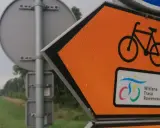 Pomarańczowy znak kierunkowy z rowerem i napisem "Wiślana Trasa Rowerowa" zapowiada podróż ścieżką wzdłuż rzeki.
