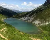 Un sentiero serpeggia tra prati verdi verso il lago Branchino, le cui acque turchesi riflettono le montagne circostanti. Alcune persone si godono un picnic sulle rive.