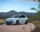 Un coche compacto Volkswagen Golf blanco circula por una carretera de adoquines con montañas rocosas al fondo.