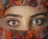 Ojos color miel que miran con curiosidad, enmarcados por un velo con estampado naranja y marrón.