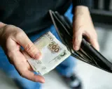 Dłonie trzymają banknoty 200 zł i pusty portfel. Może to symbolizować trudności finansowe i potrzebę wsparcia z opieki społecznej.