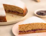 Eine köstliche, schnelle Buchweizentorte mit Marmeladenfüllung und Puderzucker bestäubt. Ein Stück auf einem rosa Teller, der Rest auf einem größeren Teller.