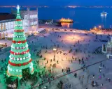 Lisbona illuminata per il weekend dell'Immacolata: un imponente albero di Natale brilla in una piazza affollata, con il fiume e le luci della città sullo sfondo.