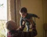 Dziadek podrzuca radosnego wnuka. Czy dziadkowie muszą płacić alimenty za syna? To pytanie, które nie ma związku z tą ciepłą chwilą.