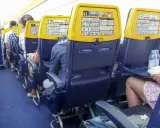 Wnętrze samolotu Boeing 737, rzędy miejsc dla pasażerów. Widok na siedzenia z żółtymi oparciami i instrukcjami bezpieczeństwa.