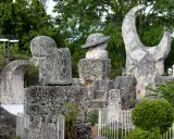 Sculture in pietra calcarea e corallo, tra cui un cappello e una forma a mezzaluna, creano un magico coral castle immerso nel verde.
