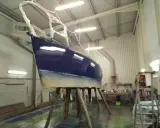 Un bateau bleu profond est en cours de stratification dans un atelier. La coque est soutenue par des tréteaux en bois.