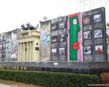 Fragment muru berlińskiego z graffiti i zdjęciami, obok replika Bramy Brandenburskiej.
