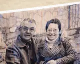 Pareja sonriente en un retrato transferir foto a madera, con un fondo de ladrillos y textura de madera visible.