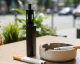 E-Zigarette und Zigaretten auf einem Tisch. Ein Aschenbecher mit glühender Zigarette. Die Wahl zwischen Raucher und Nichtraucher.