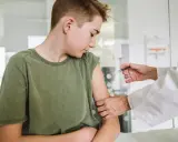 Chłopiec w zielonej koszulce otrzymuje zastrzyk od lekarza w białym fartuchu.