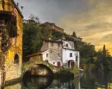 Malerische Häuser am Wasser in Nesso am Comer See, mit einer alten Steinbrücke und goldenem Abendlicht.