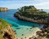 Malownicza zatoczka z turkusową wodą i piaszczystą plażą, otoczona klifami i zielenią. Idealne miejsce na relaks, jedna z pięknych palma de mallorca atrakcje.