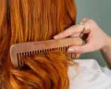 Mujer peina su cabello pelirrojo con un peine de madera. ¿En qué época del año se cae más el pelo? El otoño es conocido por ser el momento en que el cabello se cae más.