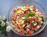 Kolorowa sałatka z kaszą bulgur, pomidorami, rzodkiewką i serem, udekorowana listkiem bazylii.
